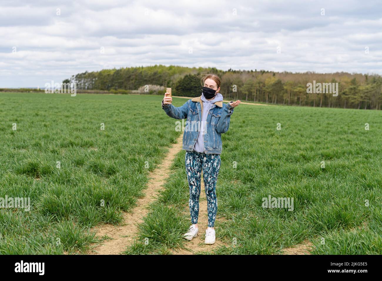 A young Caucasian woman in a black mask taking selfies in the green field Stock Photo
