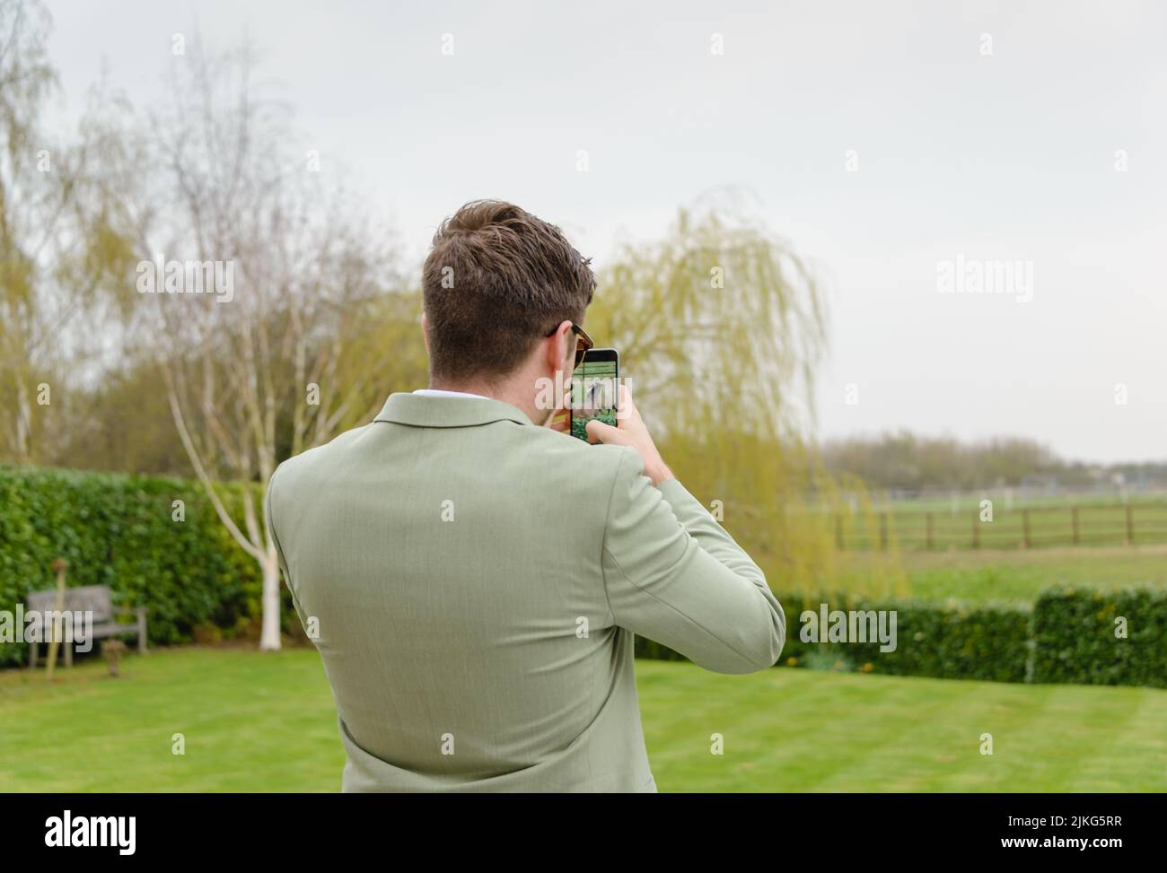 A young Caucasian man in a suit taking pictures in a green meadow Stock Photo