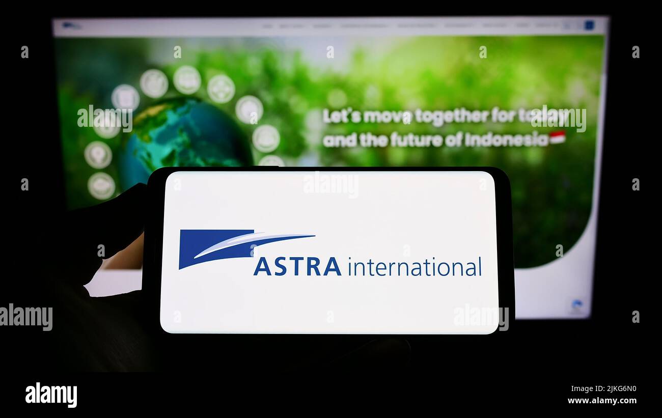 Person holding smartphone with logo of Indonesian company PT Astra International Tbk on screen in front of website. Focus on phone display. Stock Photo