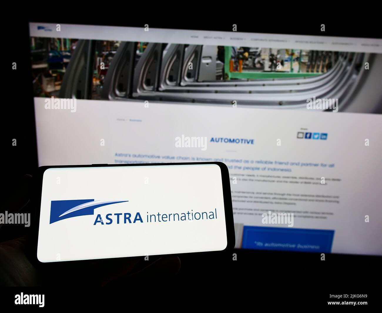Person holding mobile phone with logo of Indonesian company PT Astra International Tbk on screen in front of web page. Focus on phone display. Stock Photo