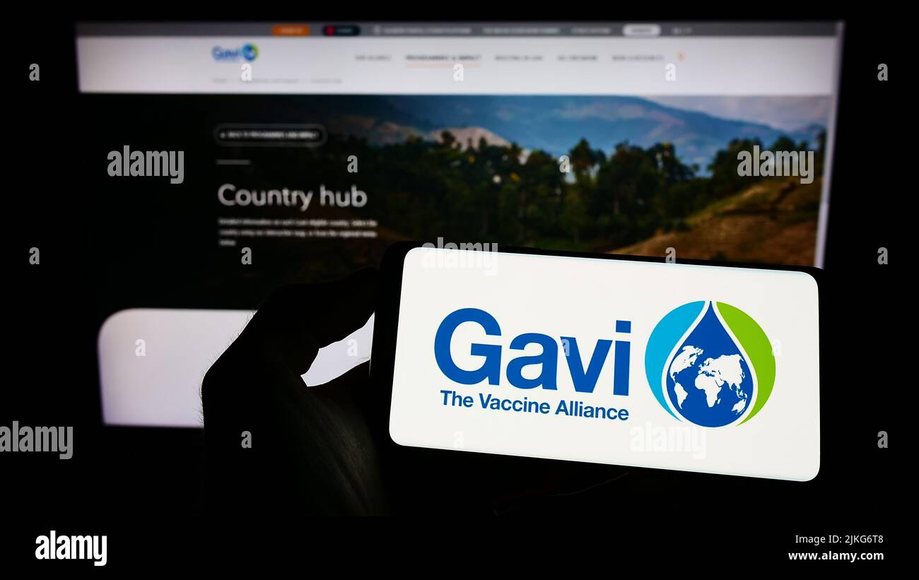 Person holding mobile phone with logo of health partnership Gavi, the Vaccine Alliance on screen in front of web page. Focus on phone display. Stock Photo