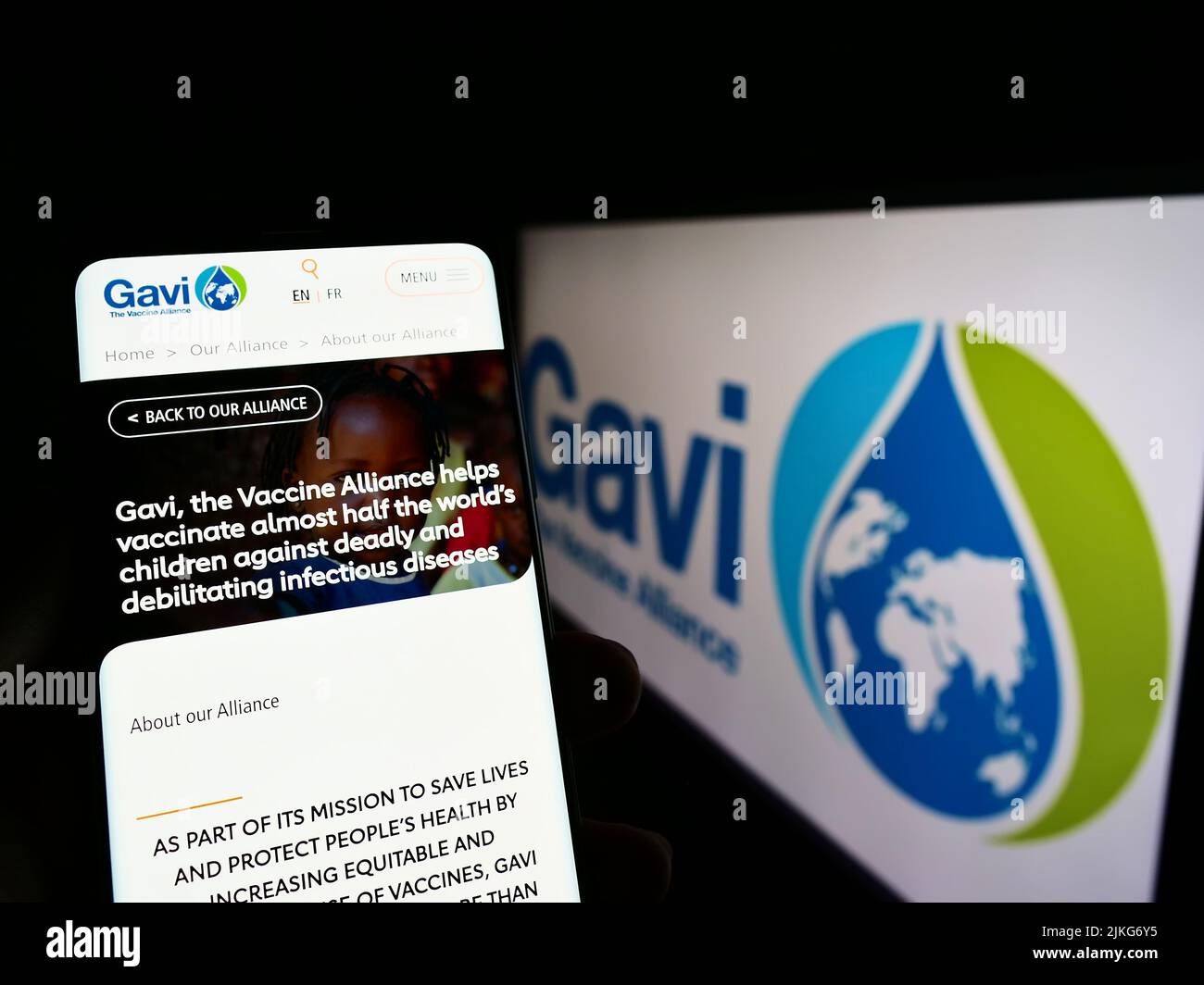 Person holding cellphone with website of health partnership Gavi, the Vaccine Alliance on screen with logo. Focus on center of phone display. Stock Photo