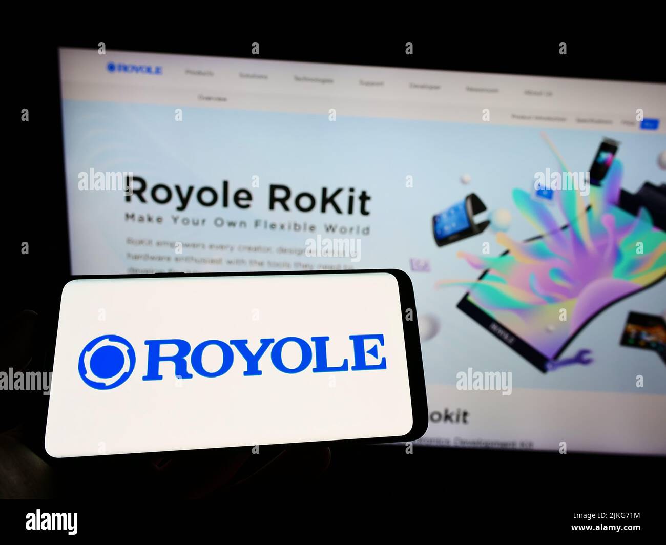 Person holding mobile phone with logo of display manufacturing company Royole Corporation on screen in front of web page. Focus on phone display. Stock Photo