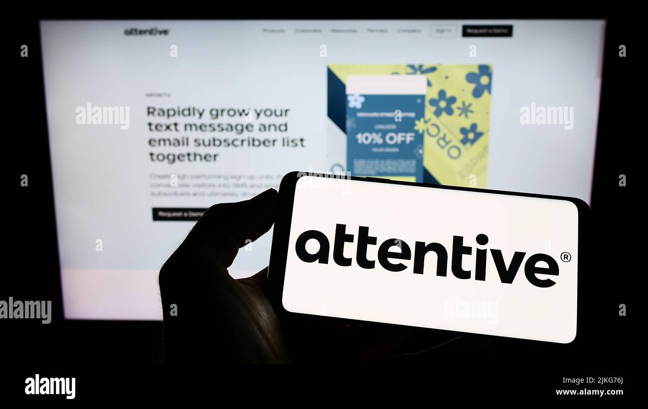 Person holding cellphone with logo of US marketing company Attentive Mobile Inc. on screen in front of business webpage. Focus on phone display. Stock Photo