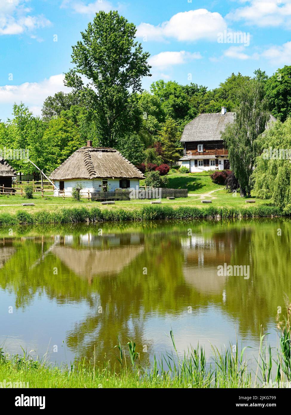Traditional wooden houses reflected in a small pond. The Open Air Folk Museum in Lublin, Poland, 03.06.2022 Stock Photo