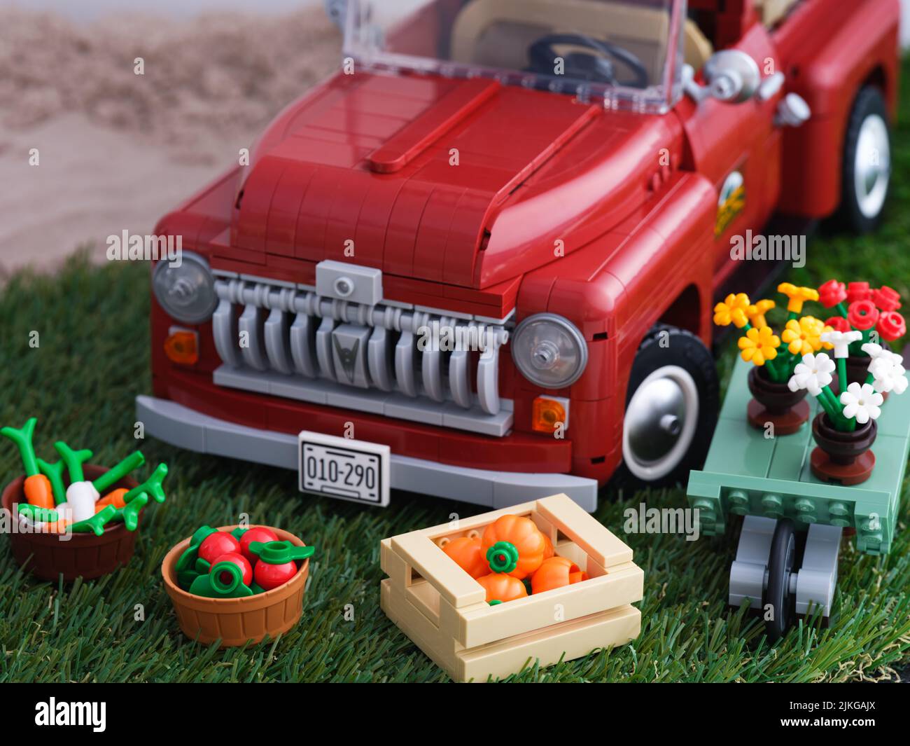 Tambov, Russian Federation - January 02, 2022 A Lego Pickup Truck and some crates of vegetables and a wheelbarrow with flowers near it on grass. Stock Photo