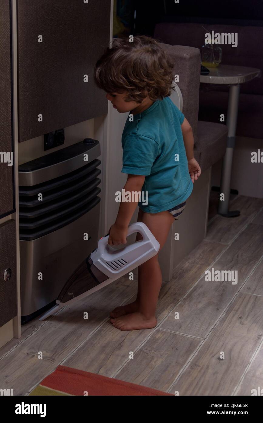 A sweet little boy vacuums the caravan while on vacation. A cute boy is ...