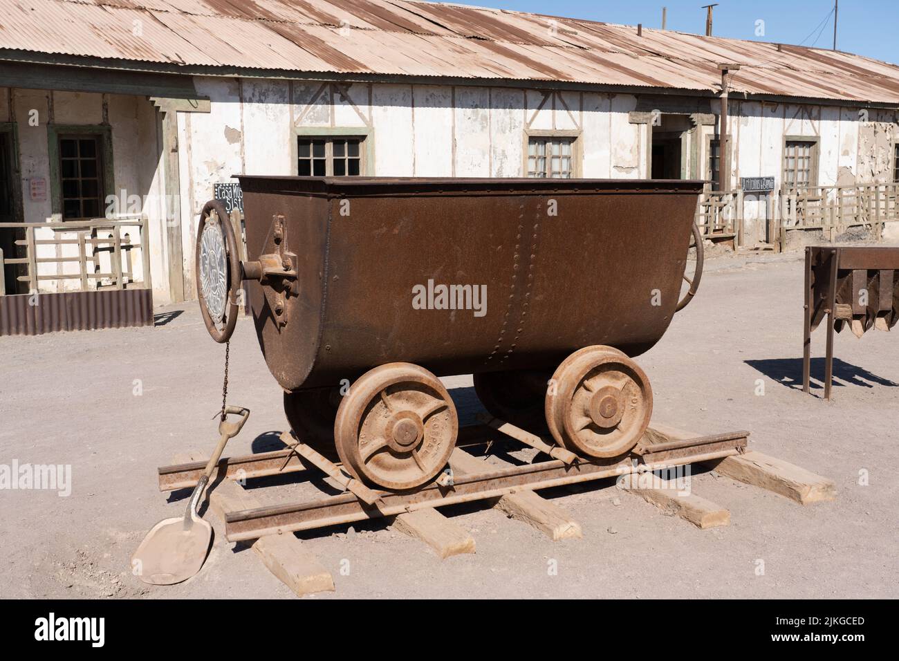 Outdoor museum display of a tipping rail cart used in the saltpeter works in Humberstone, Chile.  Employee housing behind. Stock Photo
