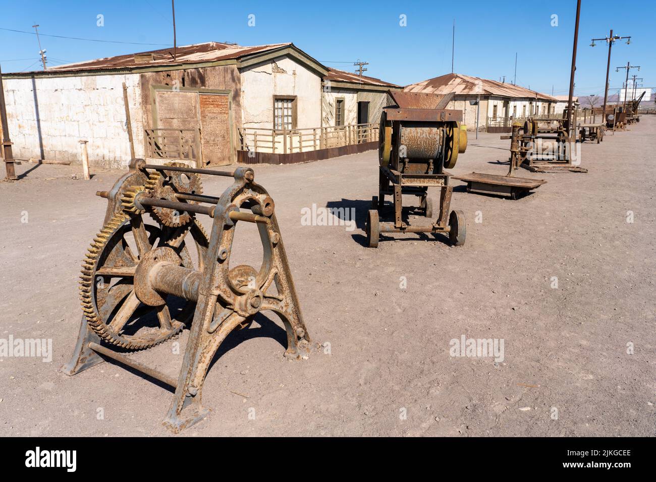 Outdoor museum display of machinery used in the saltpeter works in Humberstone, Chile.  Employee housing behind. Stock Photo
