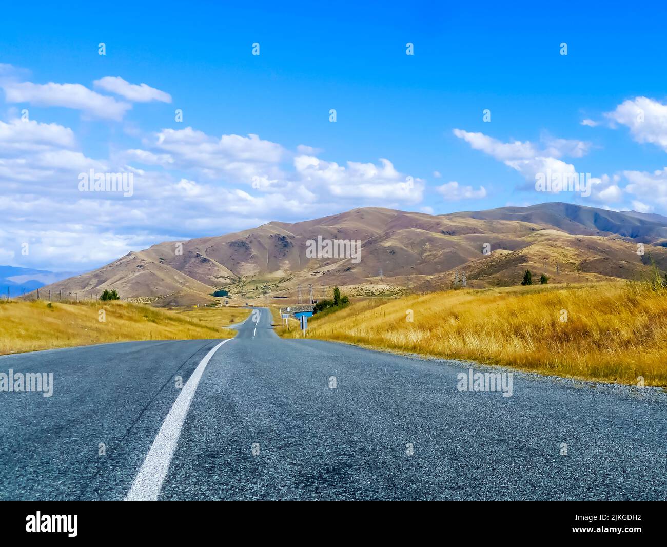 Asphalt road through a brown grass field and clouds on blue sky in