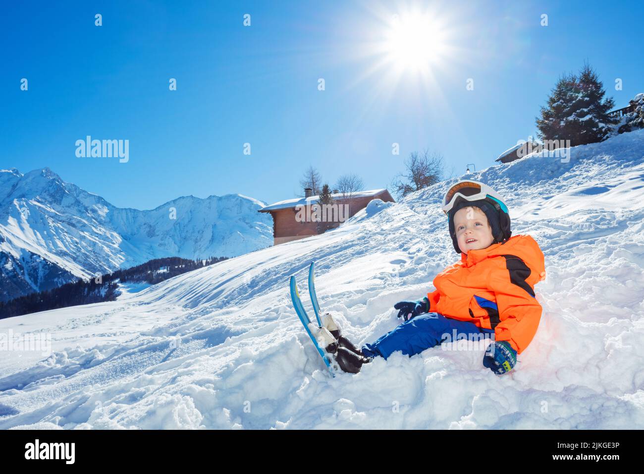 Boy with ski ready for skiing school sit in snow over mountain Stock Photo
