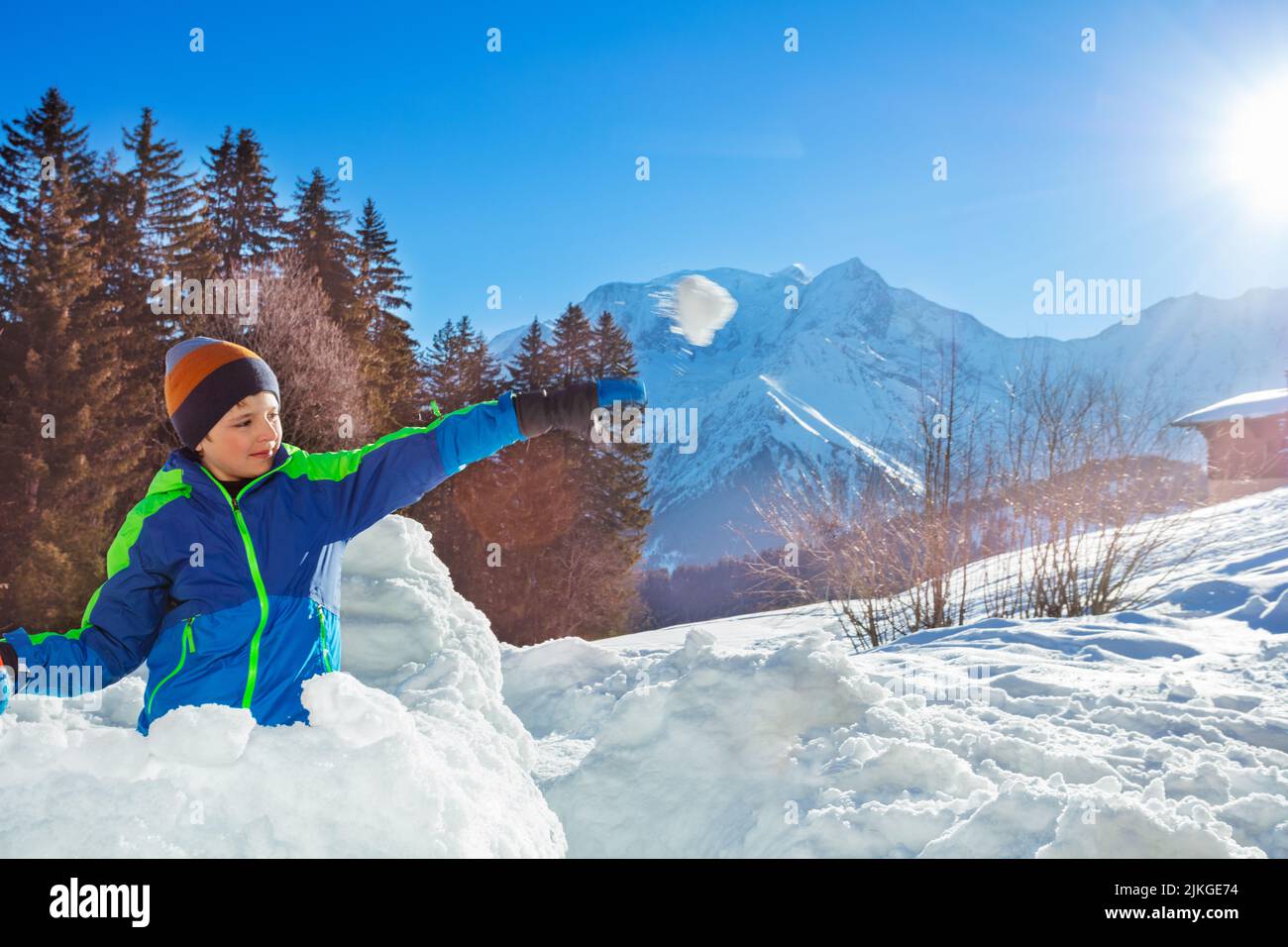 Happy boy in ski winter outfit throw snowball from fortress Stock Photo
