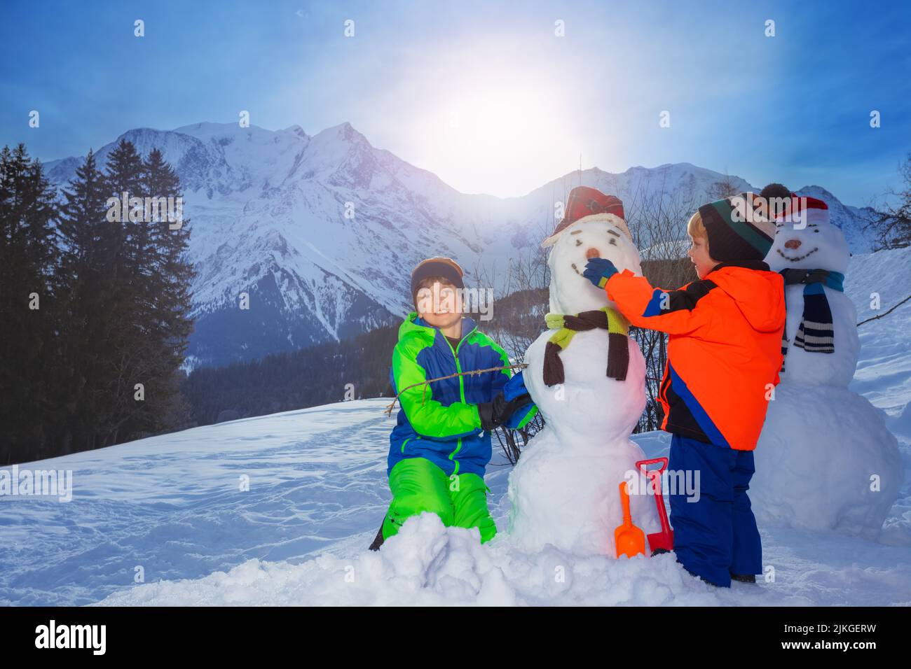 Two brothers, boys build, dress snowman outside in the mountains Stock Photo