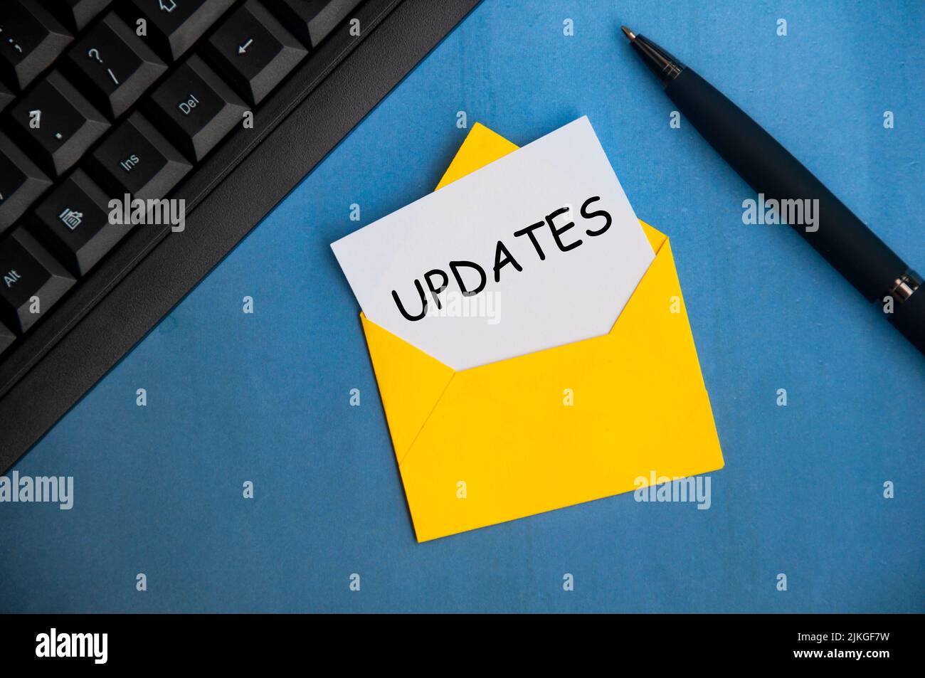 Updates text on a piece of paper in an envelope. With keyboard and pen on blue background.Business updates concept Stock Photo