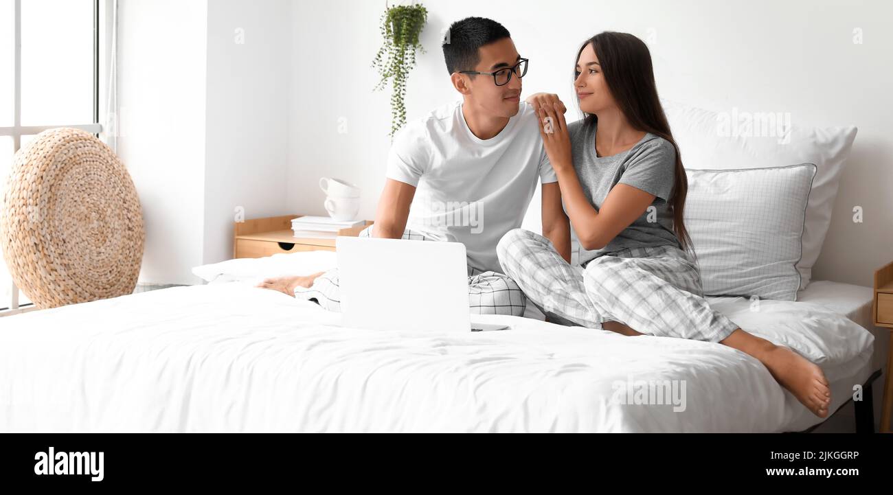 Happy young couple with laptop sitting on bed Stock Photo - Alamy