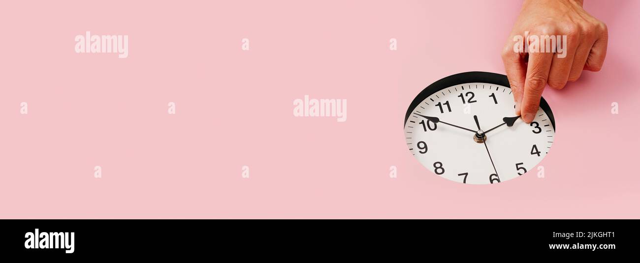 a man sets a clock backwards or forwards on a pink background with some blank space on the left, in a panoramic format to use as web banner Stock Photo