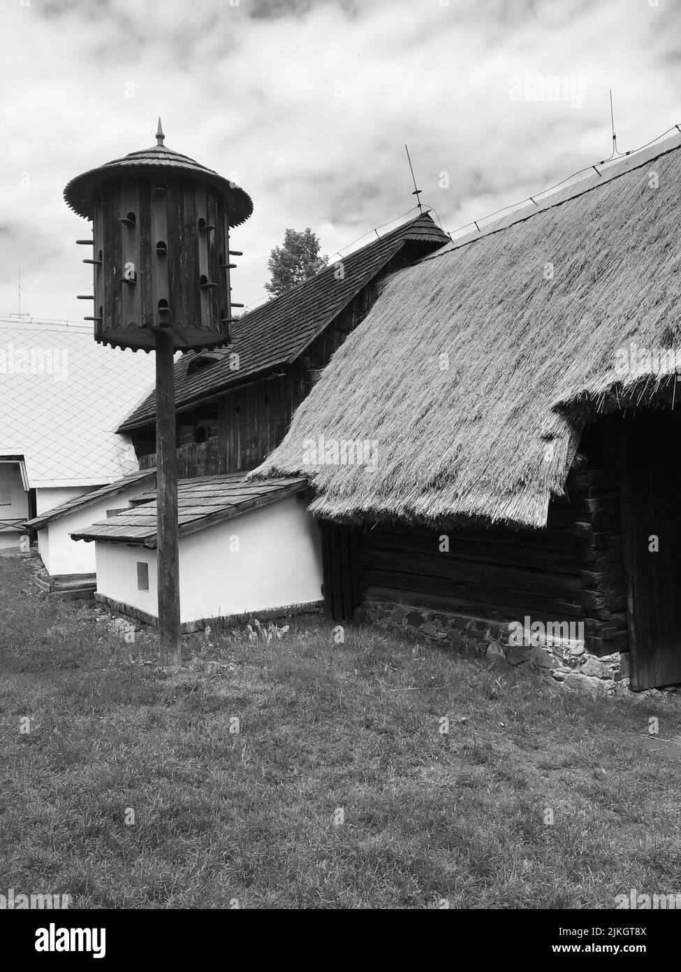 A grayscale vertical shot of a wooden dovecote next to a house Stock Photo