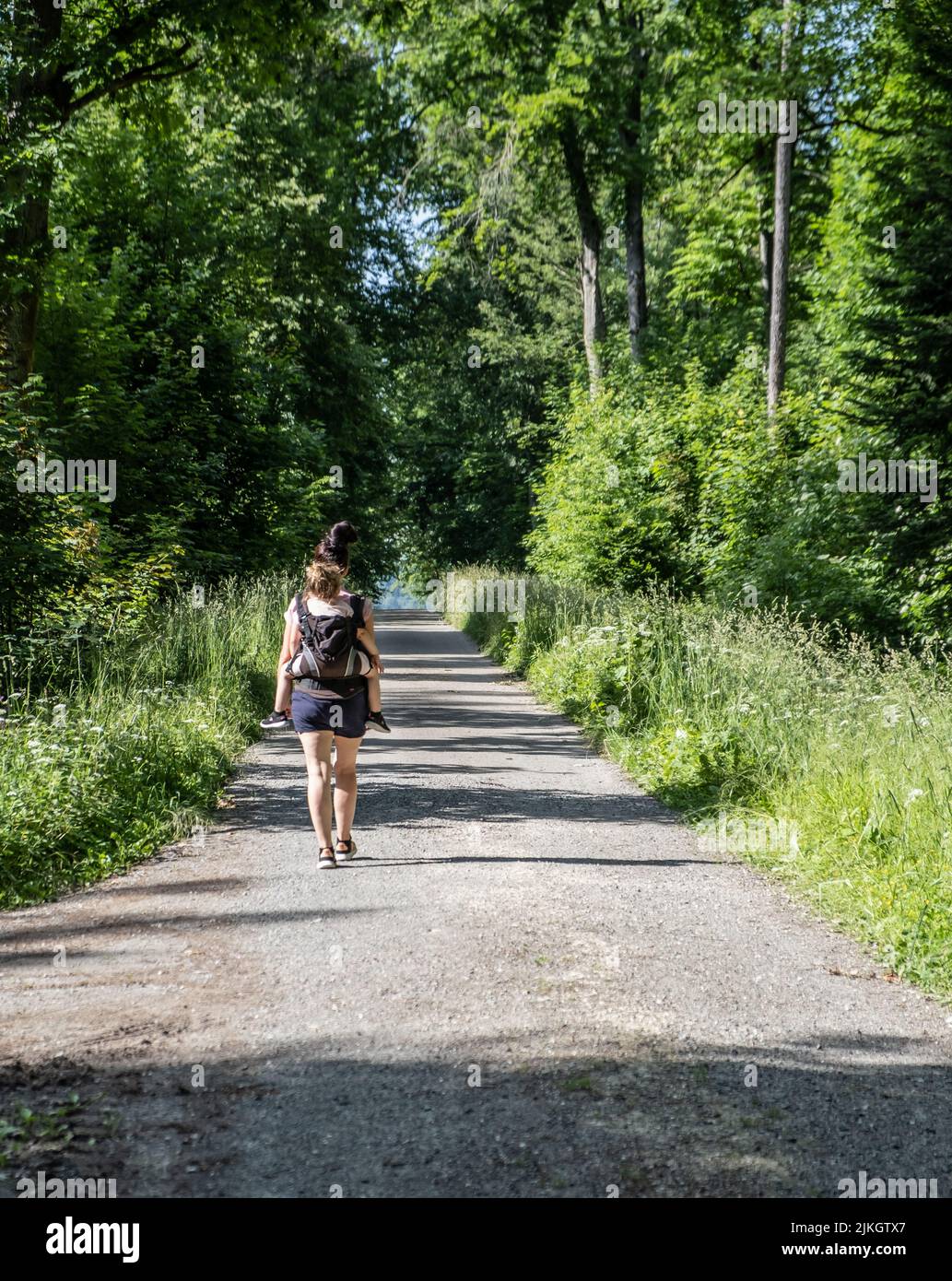 A vertical shot of a woman with her child on her back walking on a path ...