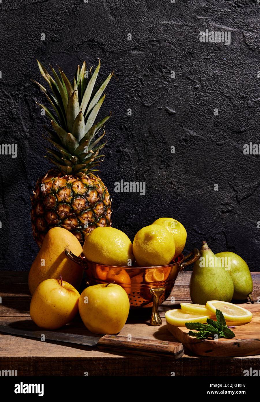 A still life, closeup of various fruit, pears, pineapple, lemons, and apples on a wooden table Stock Photo
