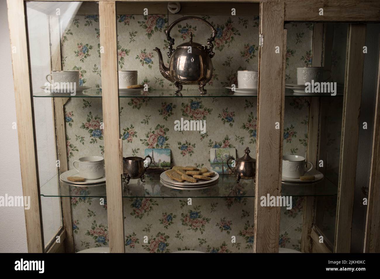 A tea set in a vintage cupboard near a floral wallpaper Stock Photo Alamy
