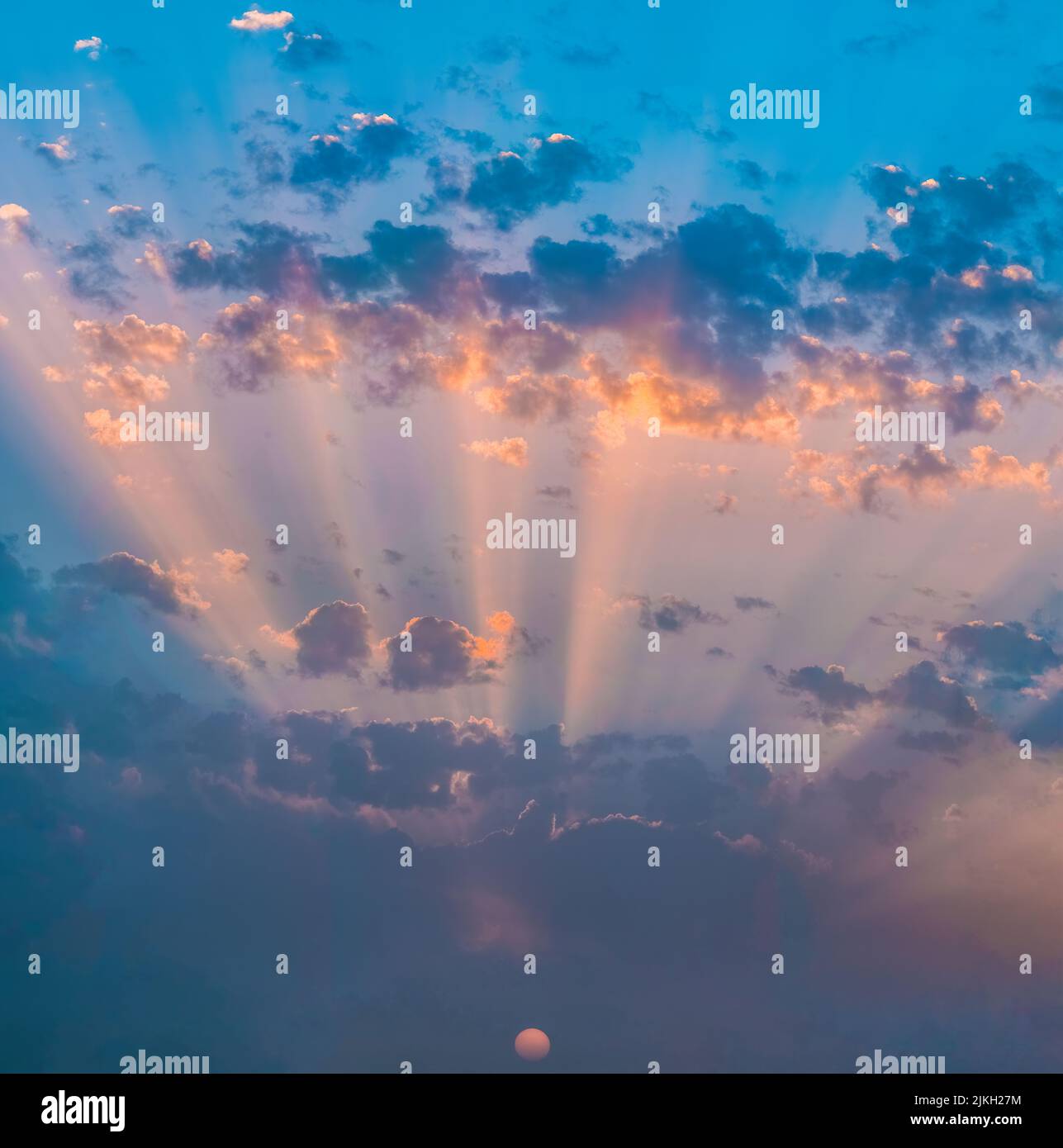 The sun rays shining in a bright blue pink sunset sky Stock Photo - Alamy