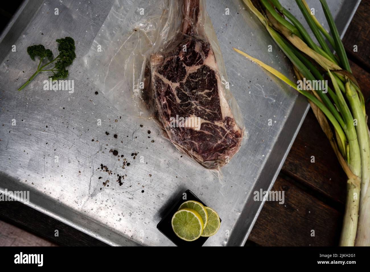 A top view of a raw slice of steak on a silver board with herbs and lemon slices Stock Photo