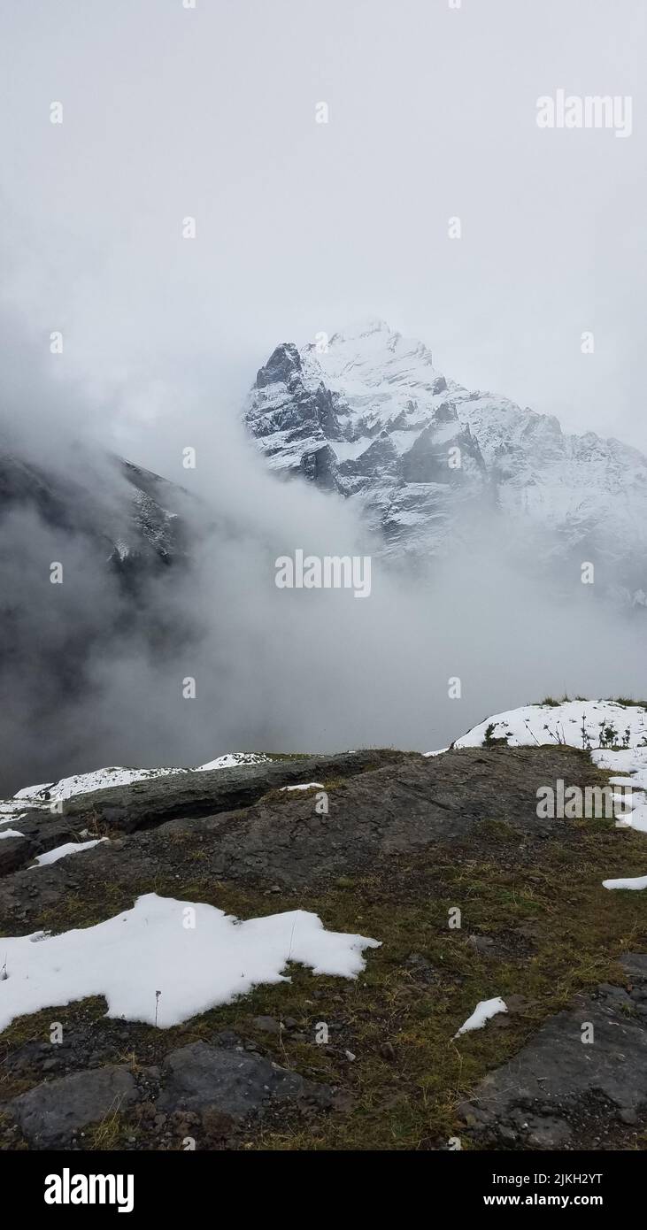 A vertical shot of the rocky mountain peak covered with clouds. Stock Photo