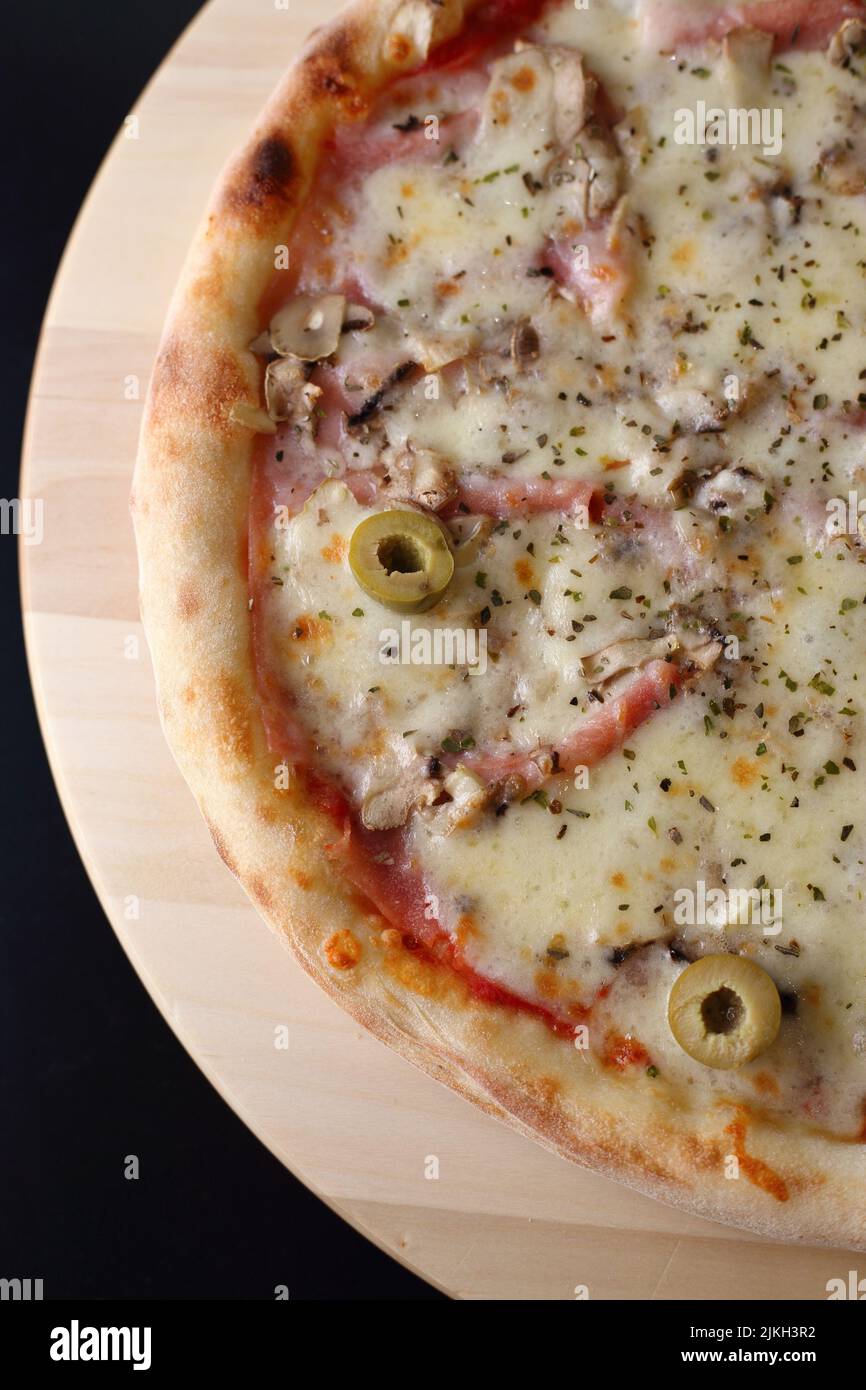 A vertical top view of a pizza with mortadella, olives, mushroom and
