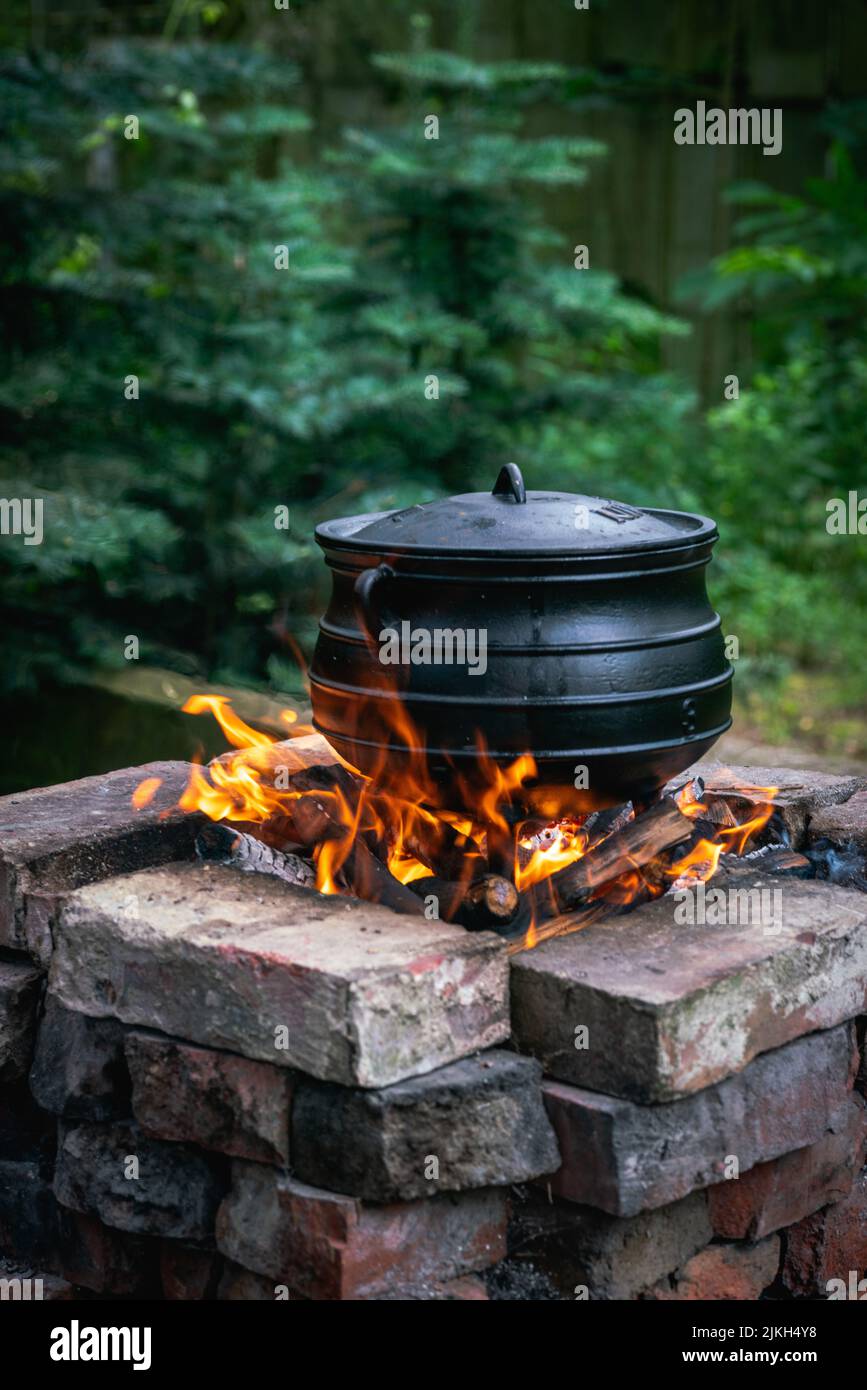 A vertical shot of an old cooking pot placed on the fire in a brick stove outdoors Stock Photo