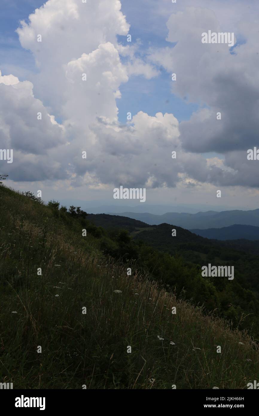 Beautiful view of the slope of green hill, mountain range covered with forest, with cloudy sky in background Stock Photo