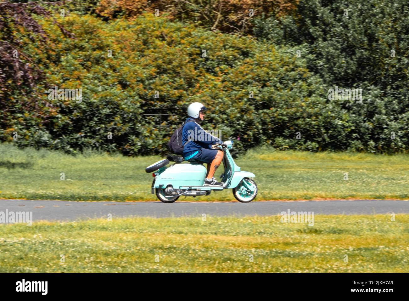 side view pan shot of man riding classic light green innocenti lambretta 125 scooter moped at weston park classic car show 2022 Stock Photo