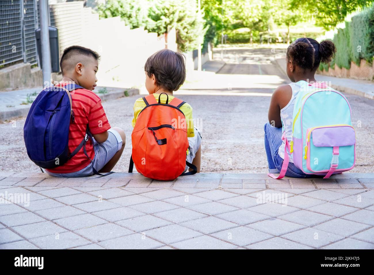multiethnic kids with backpacks sitting on the street at school entrance eating apples. Back to school concept. Multiethnic children group Stock Photo