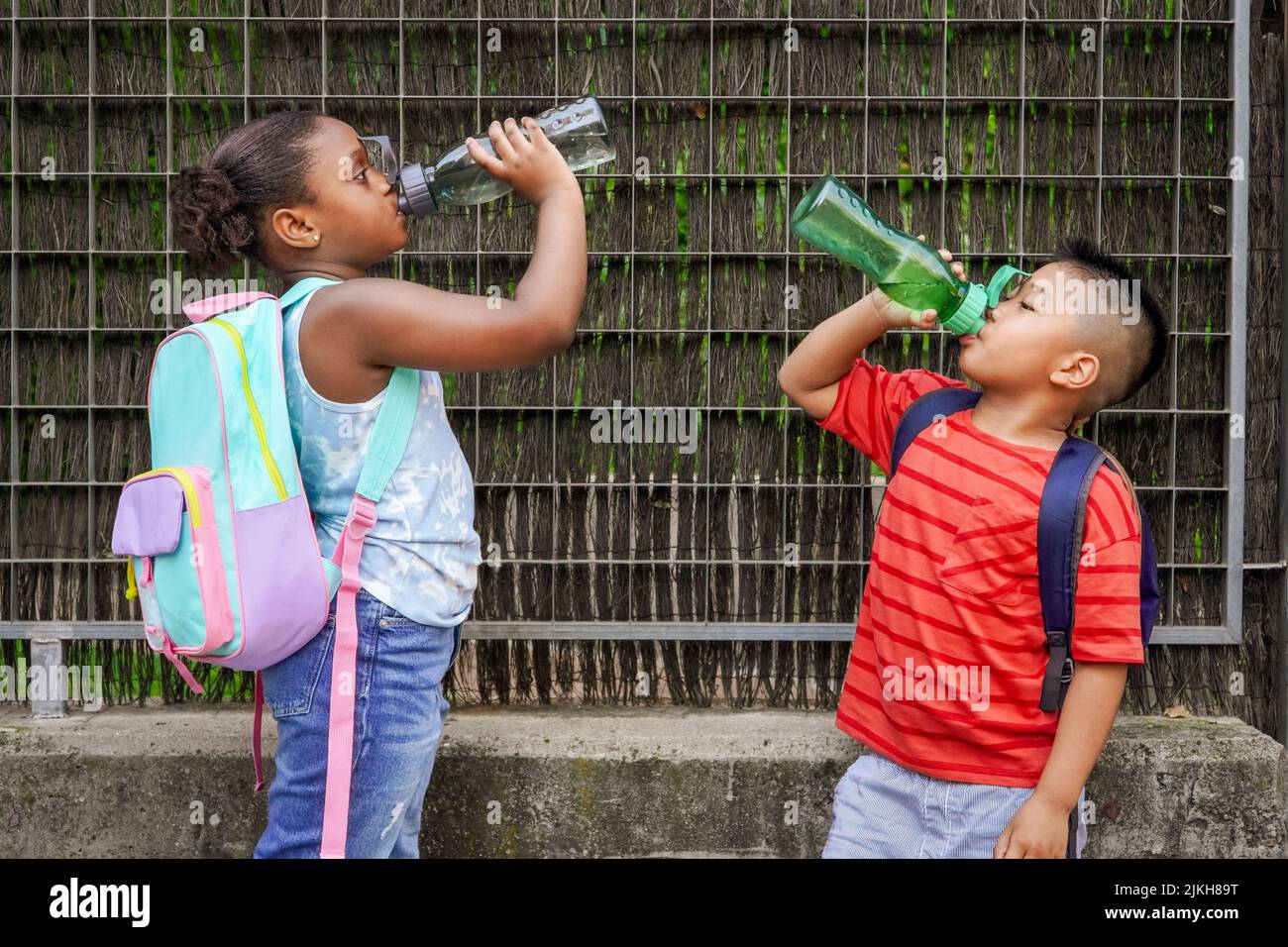 multiethnic kids with backpacks drinking water at school entrancce. Back to school concept. Multiethnic children group shooting Stock Photo