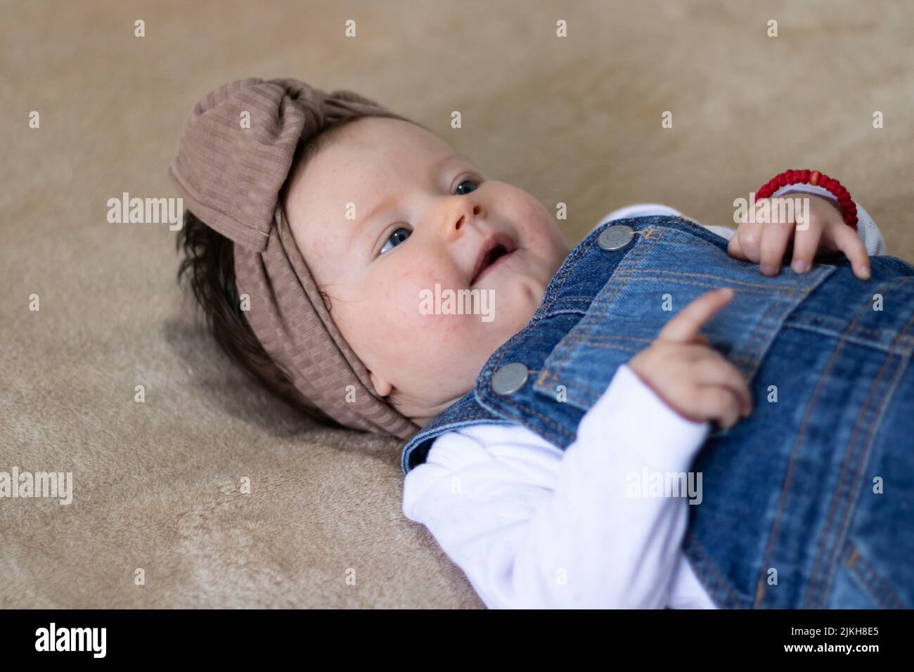 A closeup portrait of a cute Caucasian baby girl with a brown knot turban, lying in bed Stock Photo