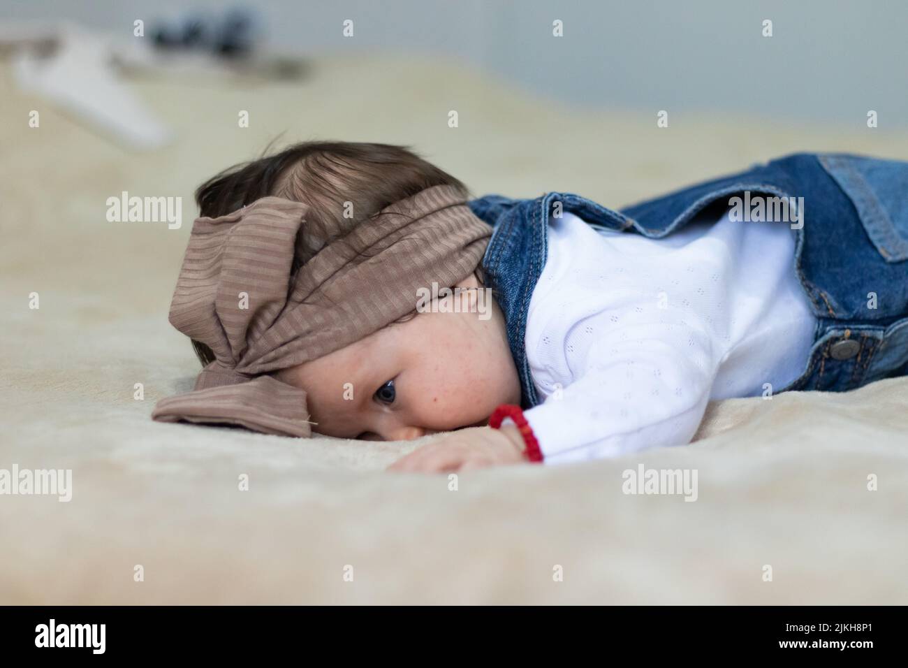 A closeup portrait of a cute Caucasian baby girl with a brown knot turban, lying in bed Stock Photo