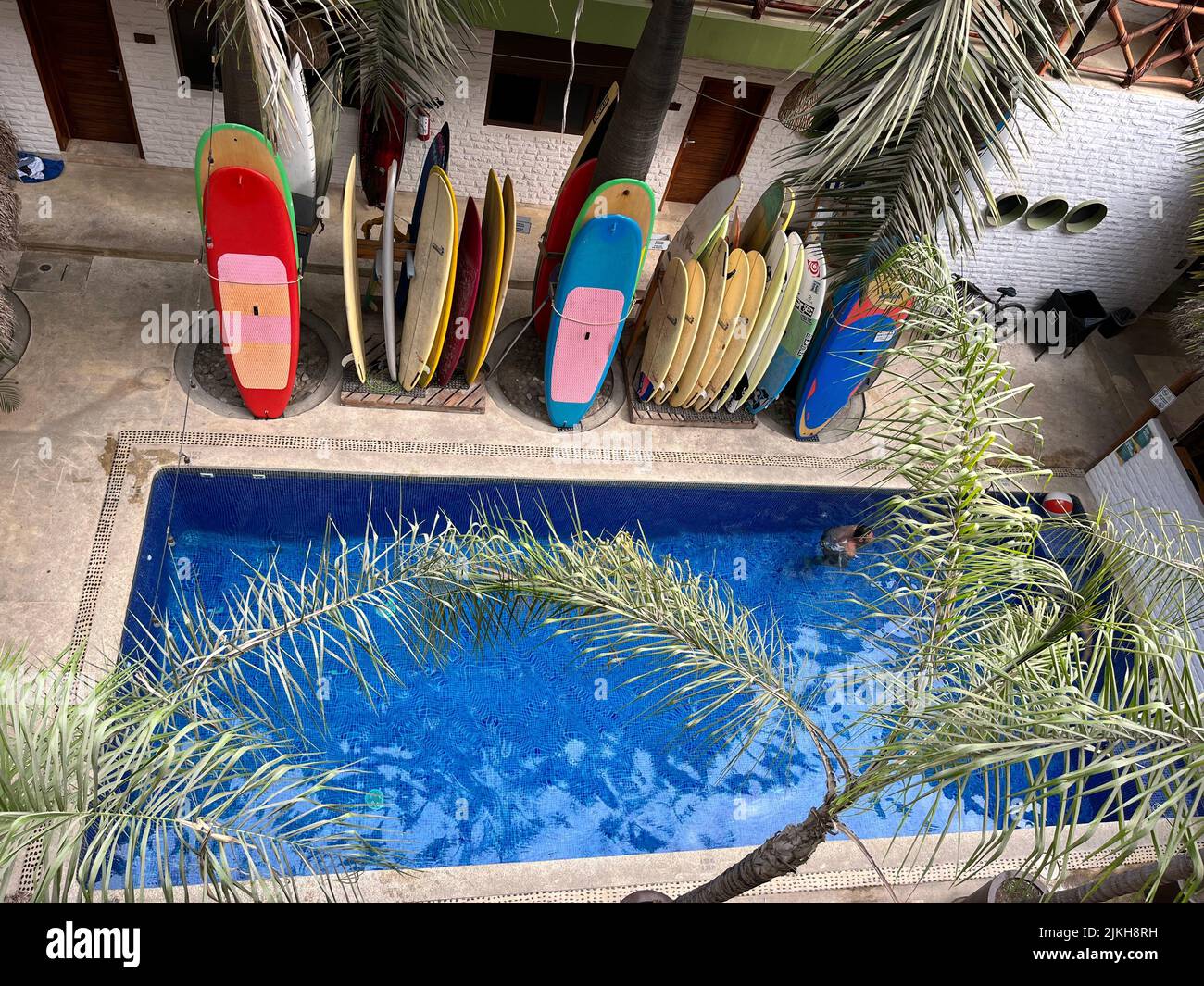 Surfboards rest stacked side by side next to a blue pool, white walls, and palm trees in a hotel at Sayulita Mexico, Nayarit Stock Photo