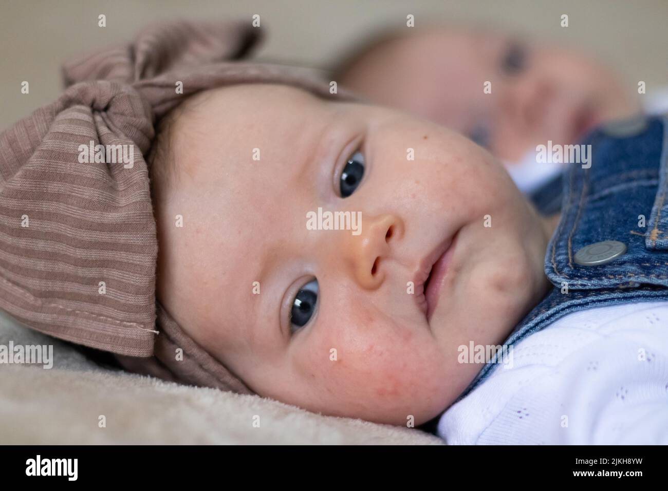 A closeup portrait of a cute Caucasian baby girl with a brown knot turban, lying in bed Stock Photo