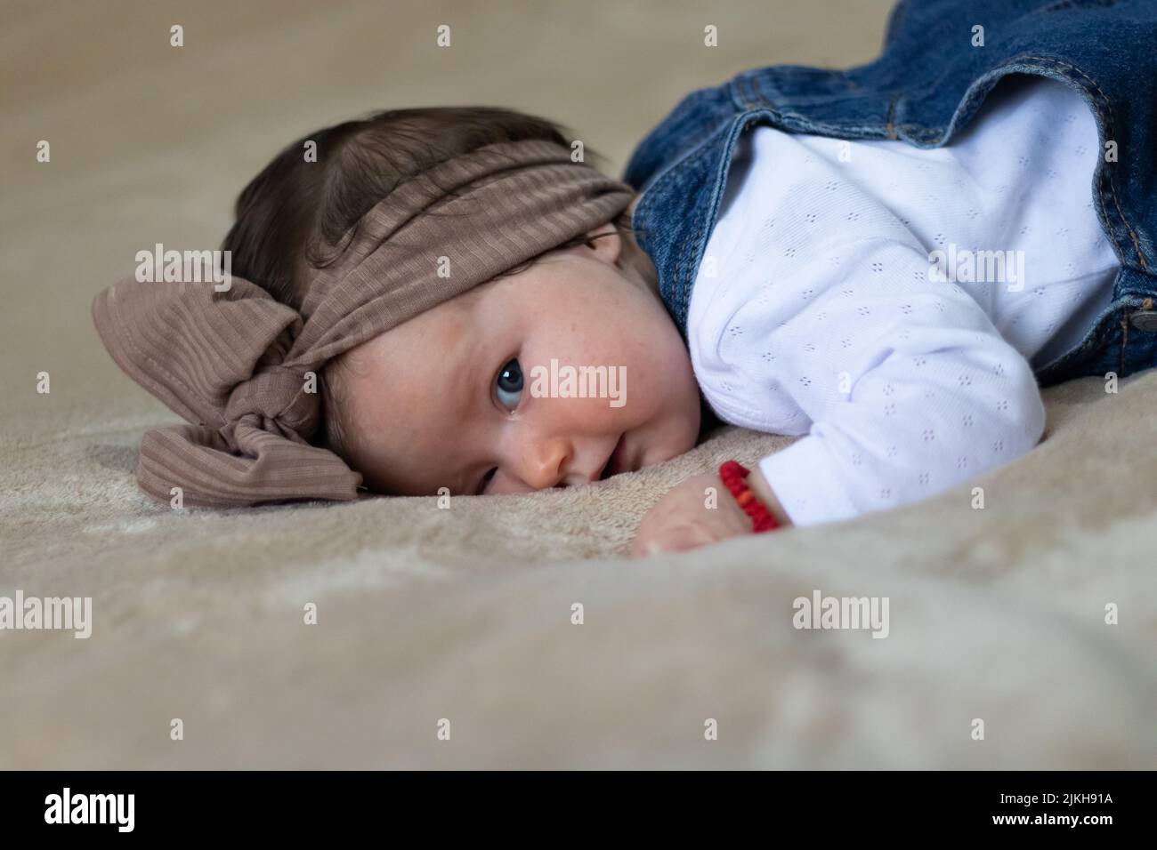 A closeup portrait of a cute Caucasian baby girl with a brown knot turban, lying in bed Stock Photo