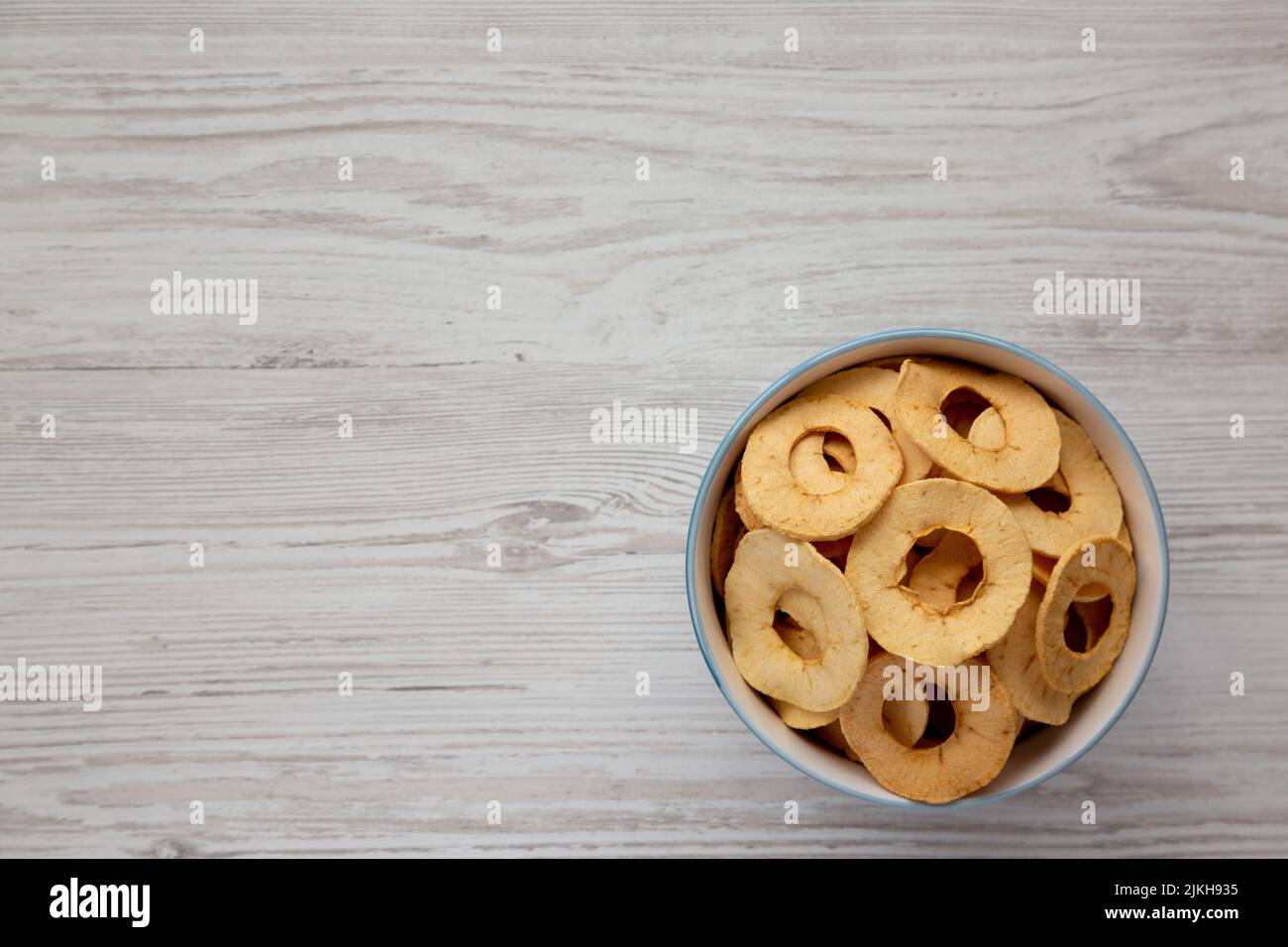 Homemade apple chips in a bowl on a white wooden background, top view. Flat lay, overhead, from above. Space for text. Stock Photo