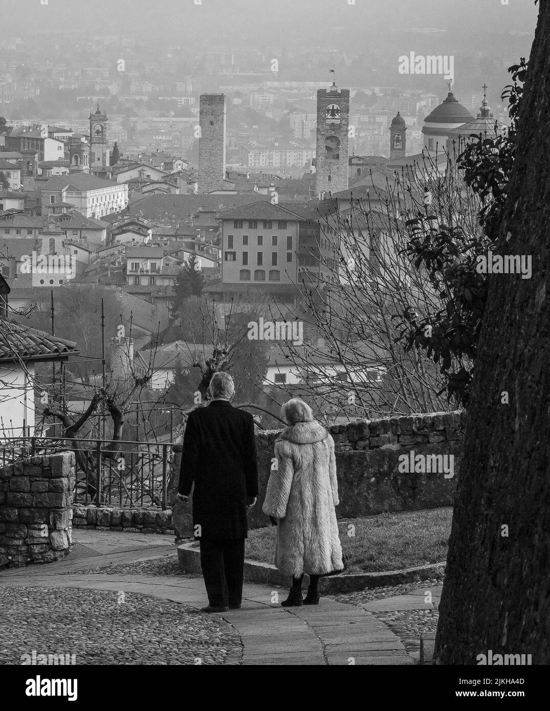 A vertical grayscale shot of a luxurious senior couple overlooking at a view from Bergamo, Italy Stock Photo