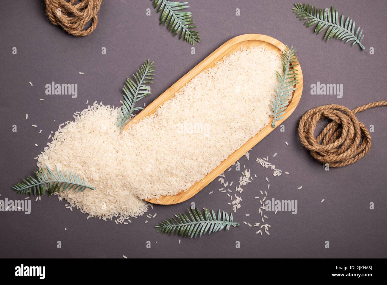 A top view of rice groats scattered on the wooden tray with a sisal rope and leaves on the table Stock Photo