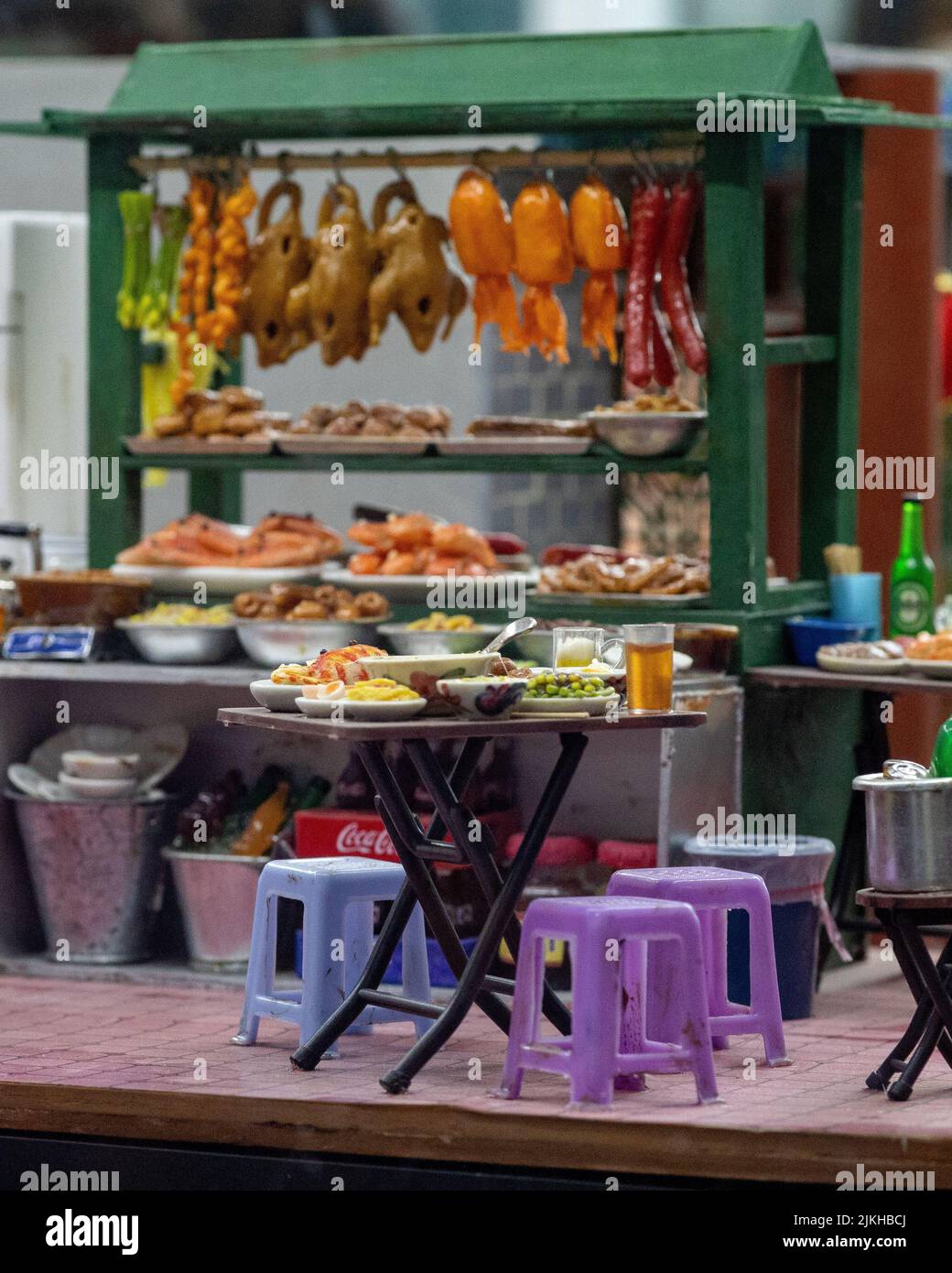 A vertical shot of a toy design of a kiosk with street food and a table with food and plastic chairs Stock Photo