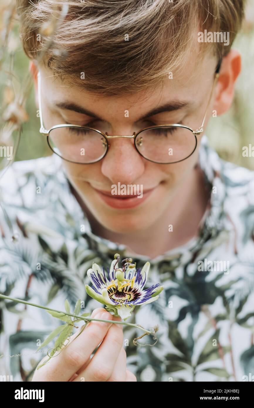 A vertical shot of a white Caucasian guy with glasses looking at a flower Stock Photo