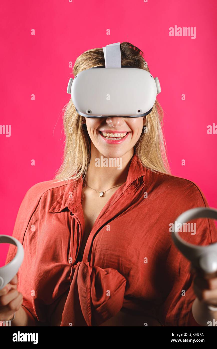 A vertical shot of a blonde caucasian girl wearing VR glasses against a vibrant pink background Stock Photo