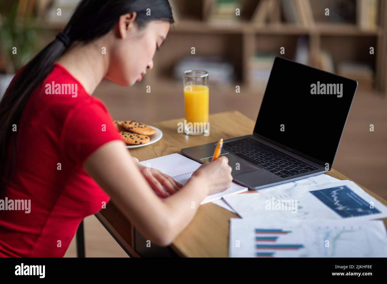 Busy young japanese female student studying with laptop with empty screen, do homework in room interior Stock Photo