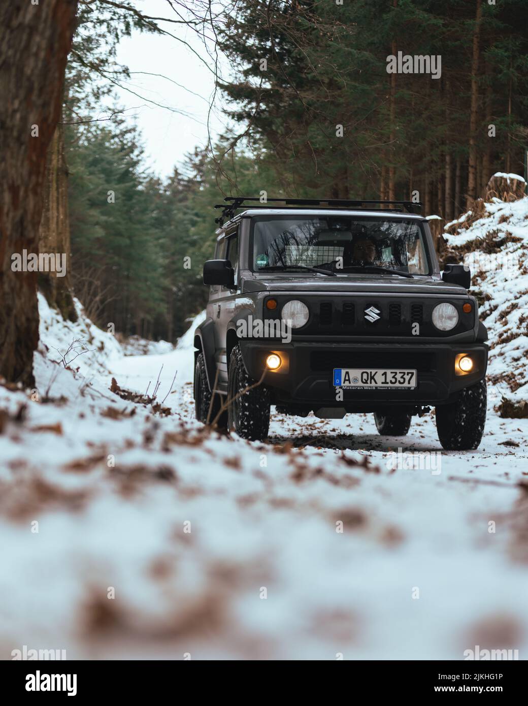 A vertical shot of black Suzuki Jimny driving through the woods in winter Stock Photo