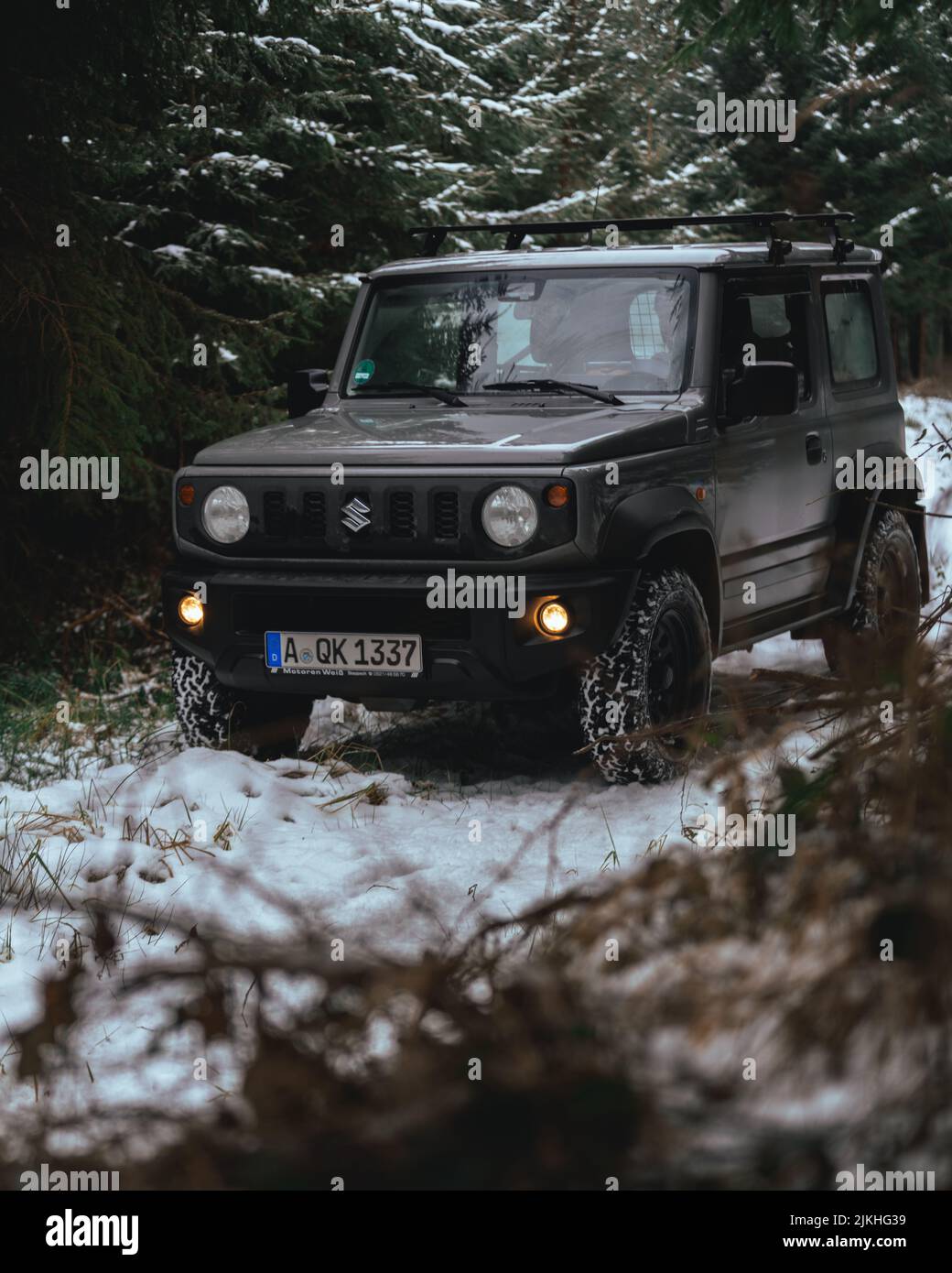 A vertical shot of black Suzuki Jimny driving through the woods in winter Stock Photo