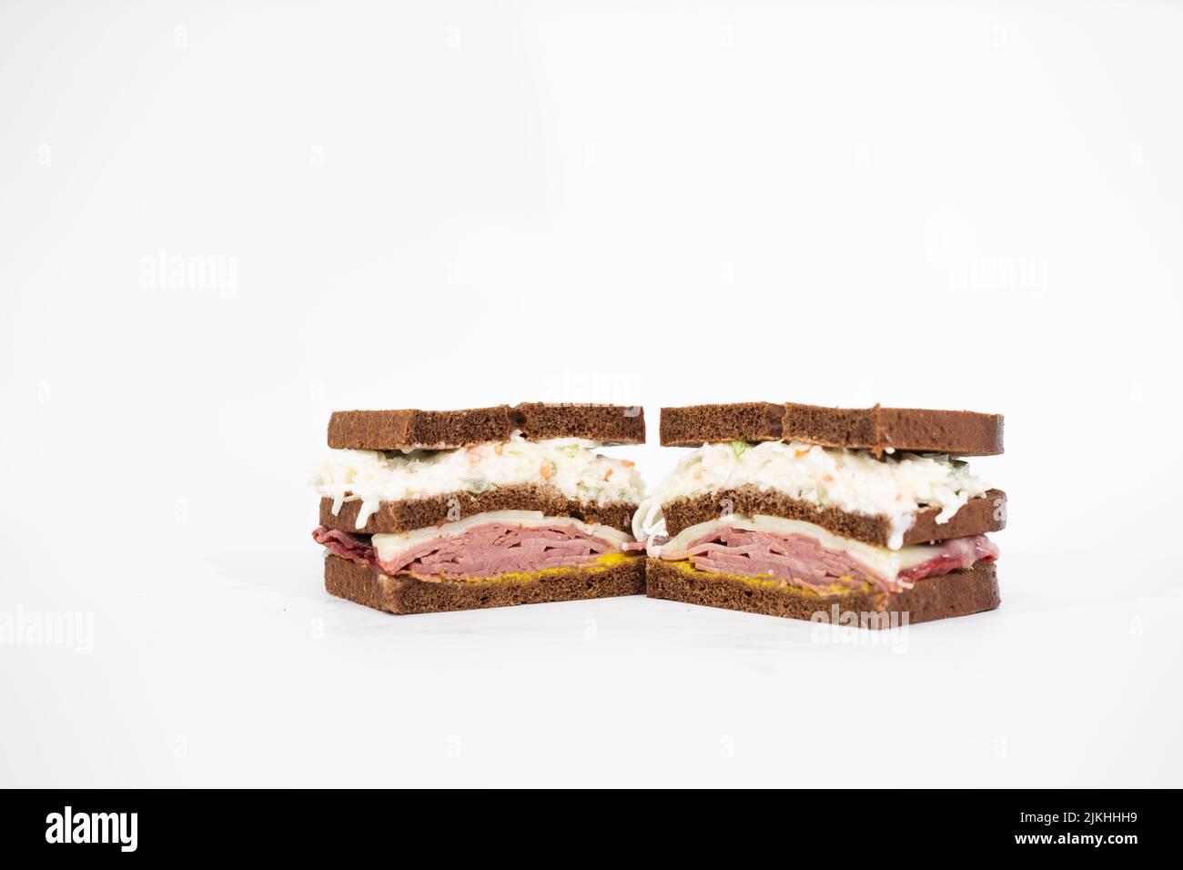 A pastrami sandwich sliced in half portraying all of its ingredients on a white background Stock