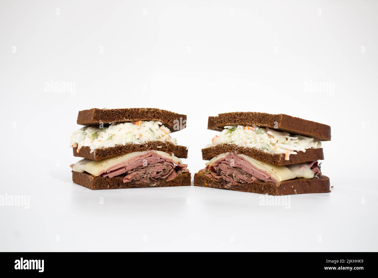 A pastrami sandwich sliced in half portraying all of its ingredients on a white background Stock