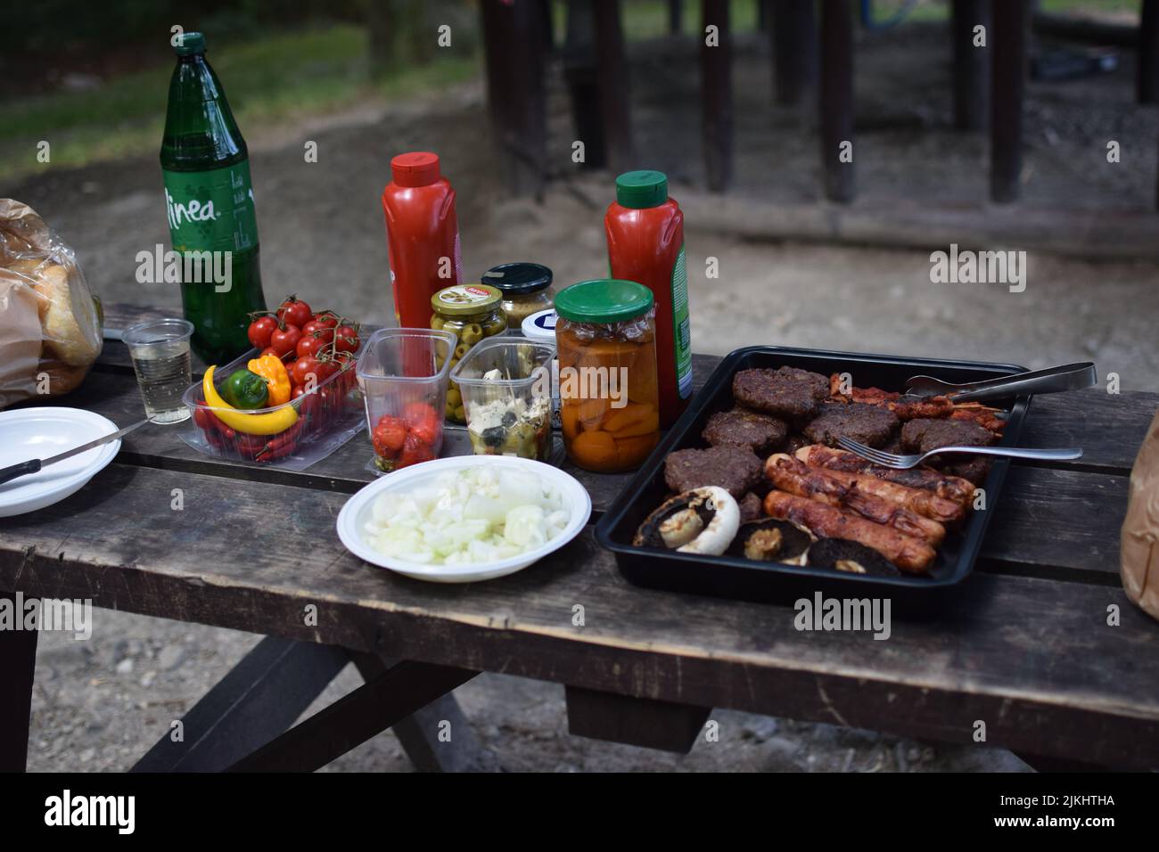 A wooden picnic table with barbecued meats, vegetables, and sauces Stock Photo